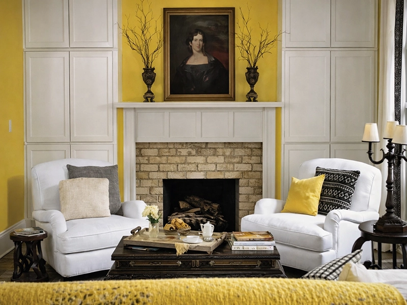 Светлый интерьер с белыми стенами, оранжевыми стульями у стола и ярким диваном в солнечной гостиной.