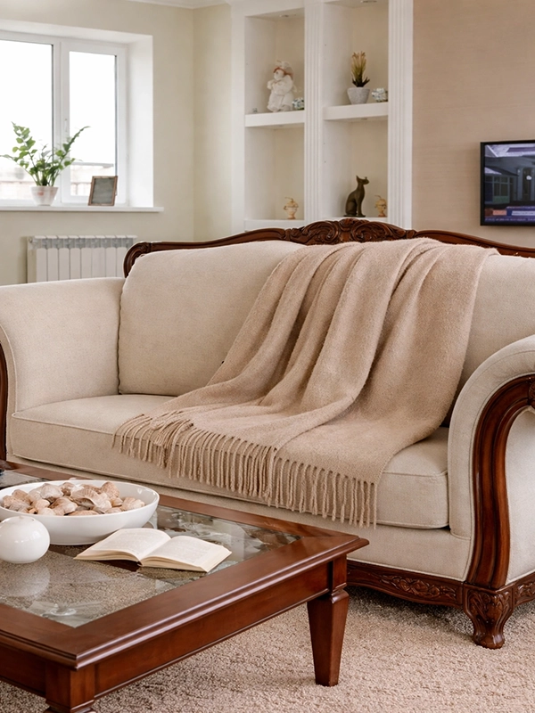 Светлый вязаный плед бежевого цвета, аккуратно наброшенный на спинку мягкого дивана в интерьере