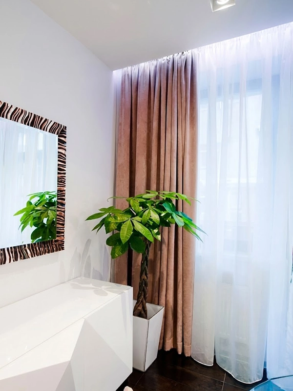 Интерьер спальни с комодом, круглым зеркалом на стене, высоким напольным цветком и шторами с подсветкой